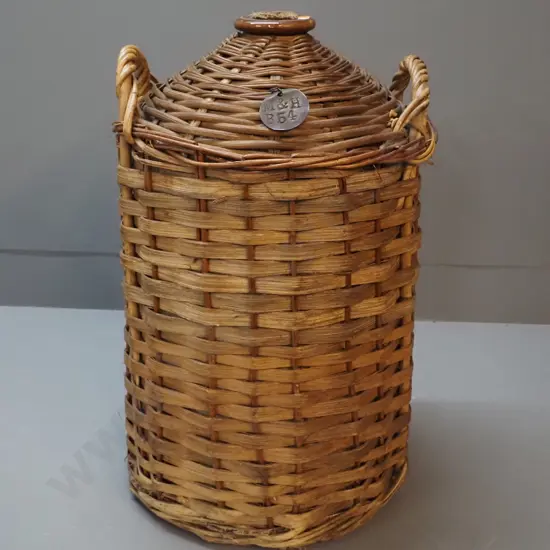 narrow-mouth stoneware crock in cane basket cover, with cork stopper and metal tag stamped 'M&H B54' H550