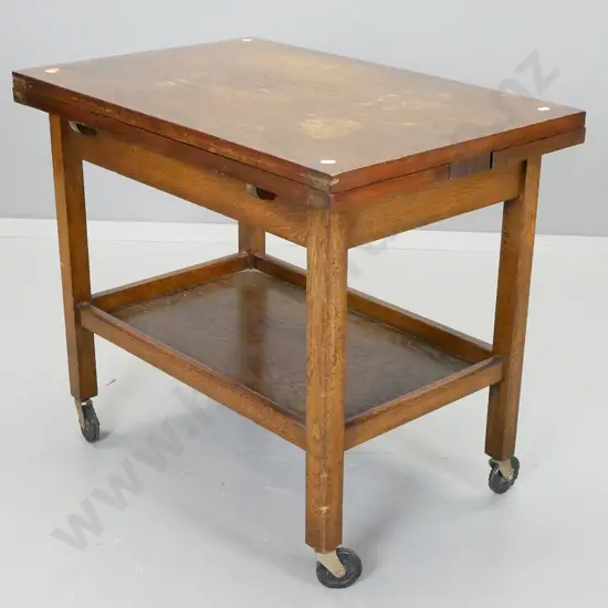 oak draw-leaf 2-tier tea trolley on black plastic casters - wear / staining to top centre section. H-640 L-730 W-890 ext