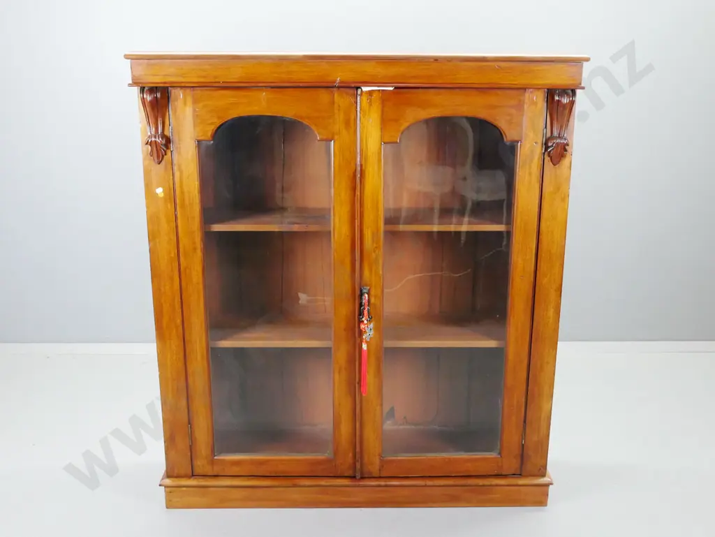 Victorian mahogany bookcase with 2 glazed arched panelled doors, carved corbels, 2 shelves, plinth base. Missing piece Image 1++