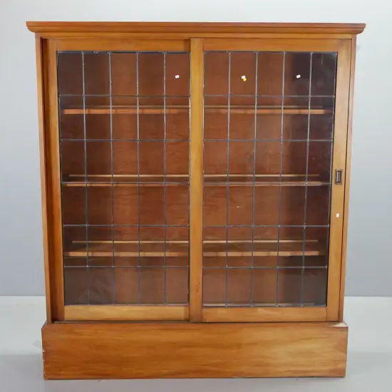 arts & crafts style rimu 3-shelf bookcase with 2 sliding leadlight doors, shaped cornice top and large plinth base.