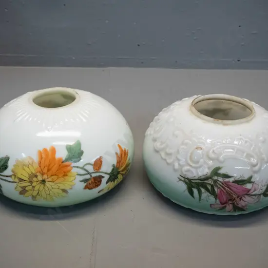 two deco hand-painted-over-transfer milk glass light shades - floral motifs on green, one with chips inside bottom rim.