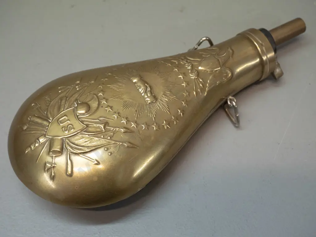 reproduction pressed brass powder flask with "US" and various insignia L-230 W-100 Image 1++