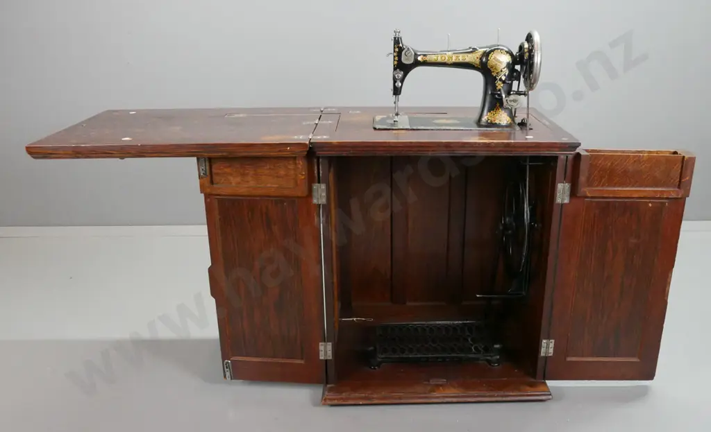 vintage Jones treadle sewing machine in figured oak cabinet with fold-out top linked to lift mechanism, 2 doors Image 1++