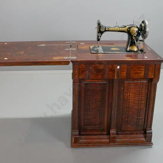 vintage Jones treadle sewing machine in figured oak cabinet with fold-out top linked to lift mechanism, 2 doors
