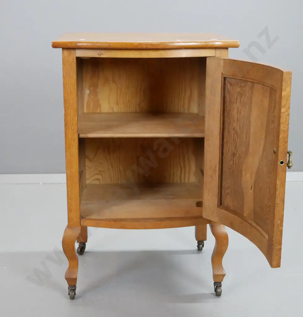 deco oak bow-front bedside cabinet with panelled door and sides, on short cab legs & metal casters, brass drop handle. Image 1++