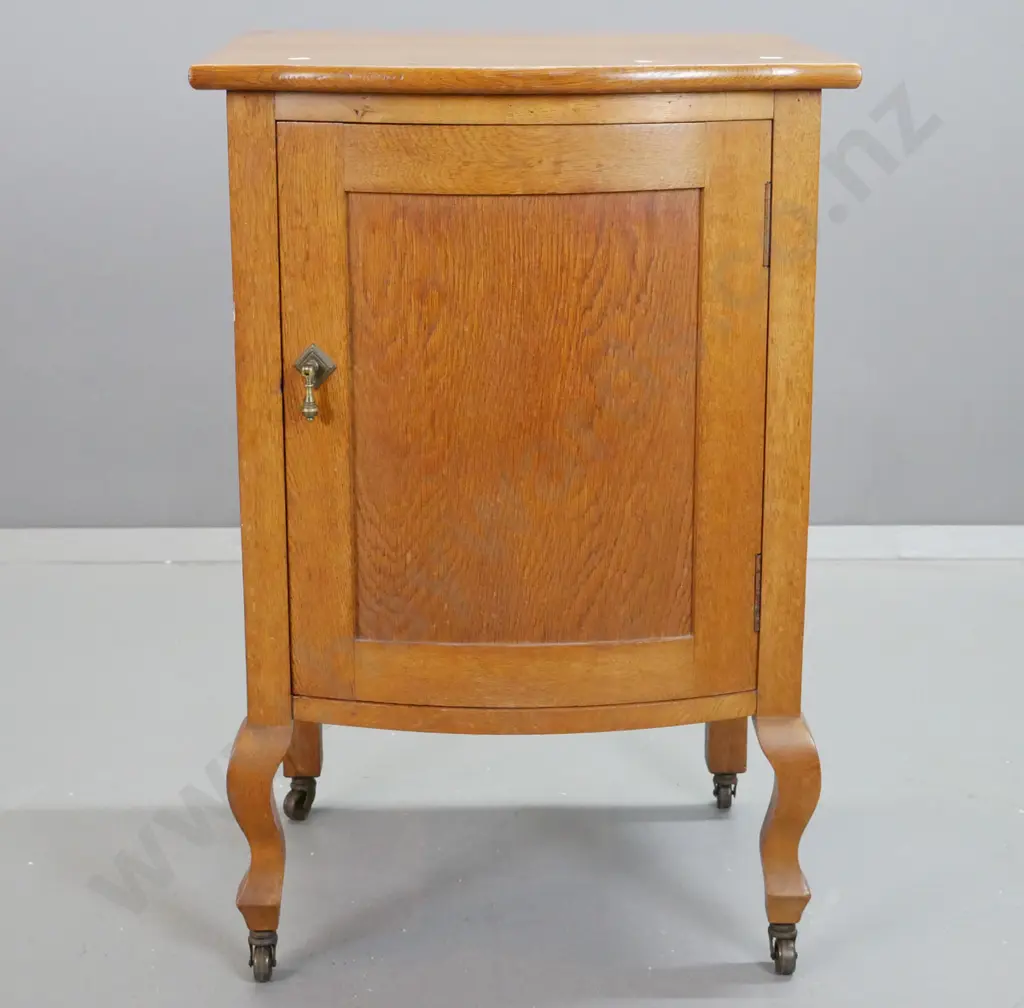 deco oak bow-front bedside cabinet with panelled door and sides, on short cab legs & metal casters, brass drop handle. Image 1++