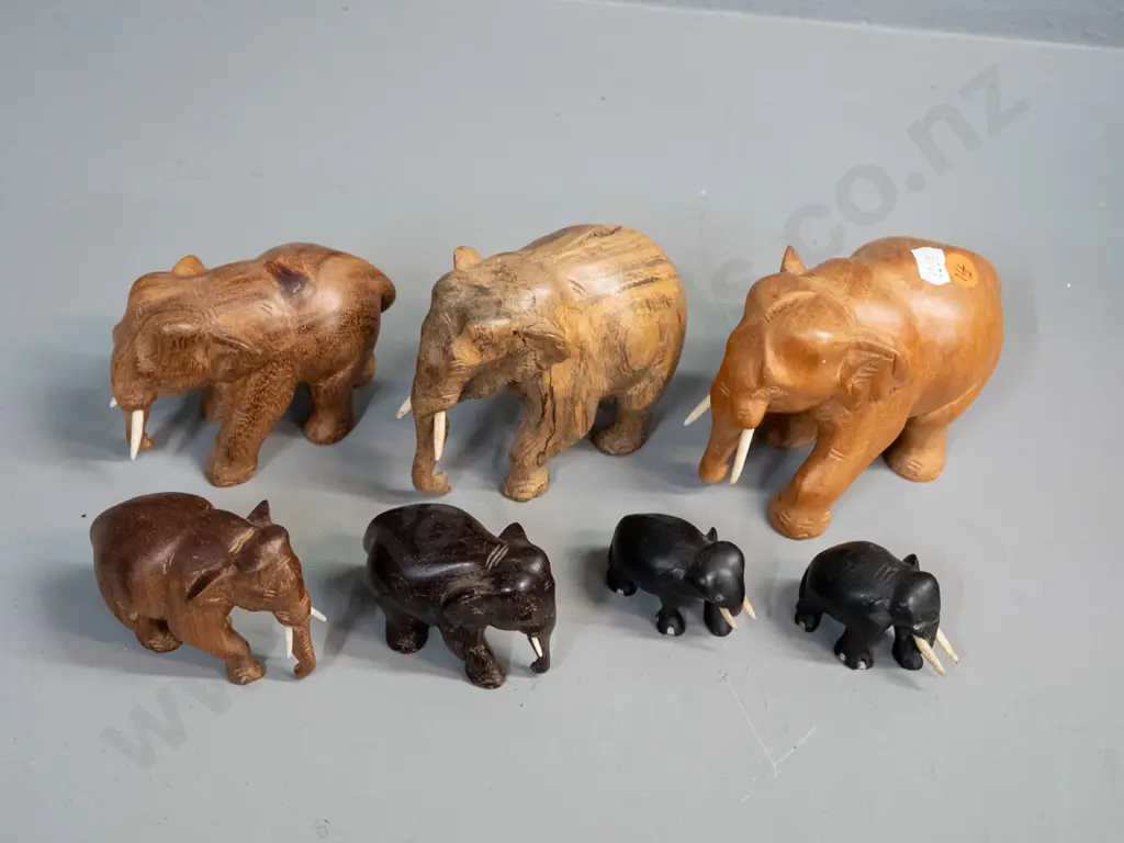 7 small carved teak, ebony and other hardwood elephants - one missing one tusk. Largest is H-95 L-110 Image 1++
