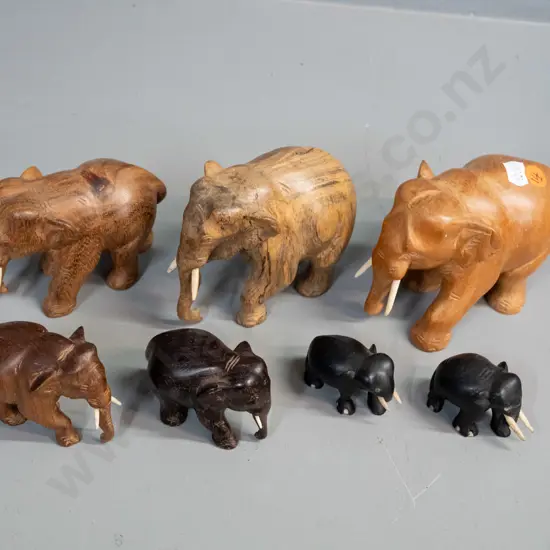 7 small carved teak, ebony and other hardwood elephants - one missing one tusk. Largest is H-95 L-110