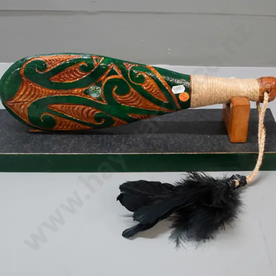 ornamental timber patu with painted decoration, paua insets, cord bound handle and black feathers, with display stand.