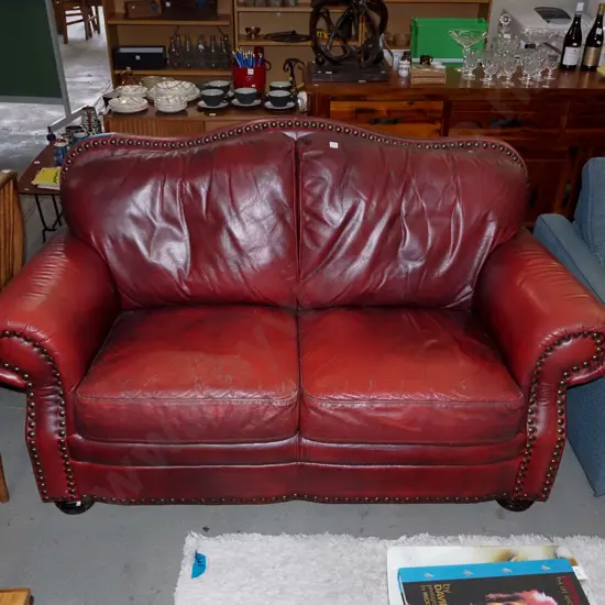 red leather rolled arm 2 seater settee with heavy dome studs -  wear and small tear to leather 