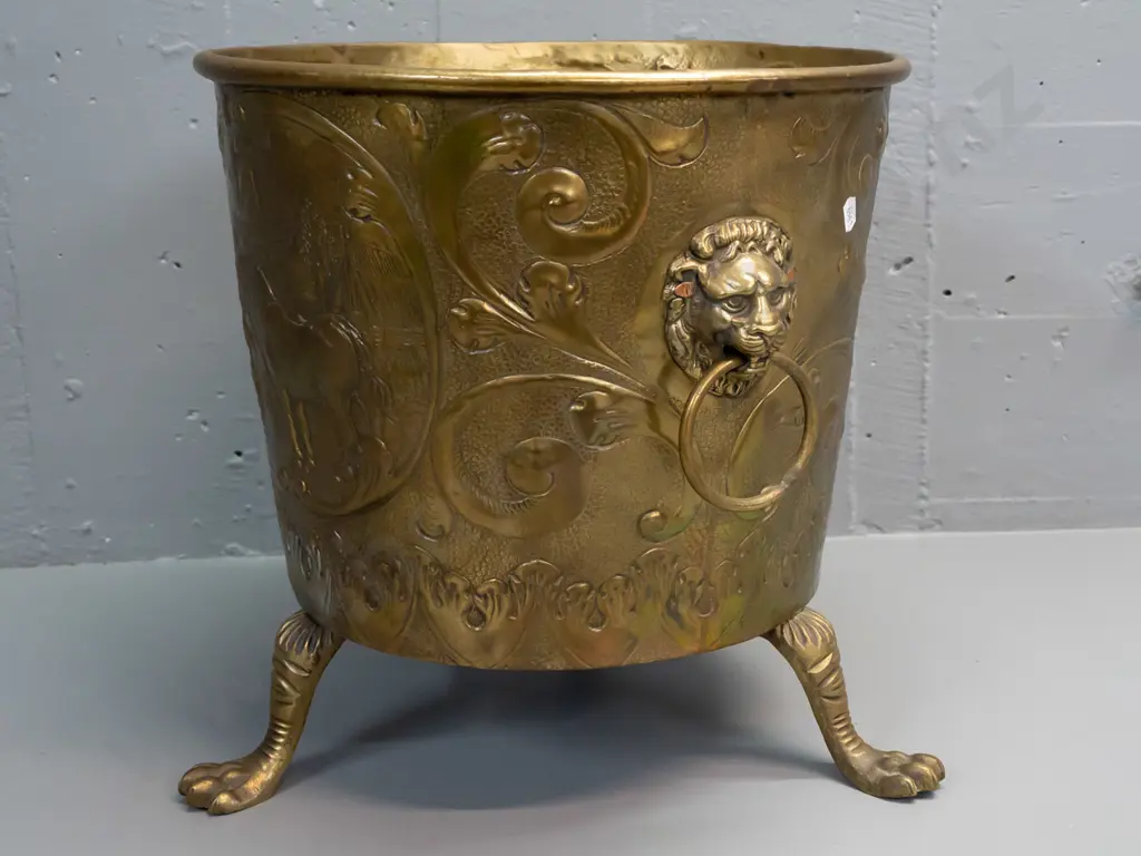beaten brass jardiniere or wood bin with horse, windmill and heraldic motifs, with lion's head ring handles, on cast paw Image 1++