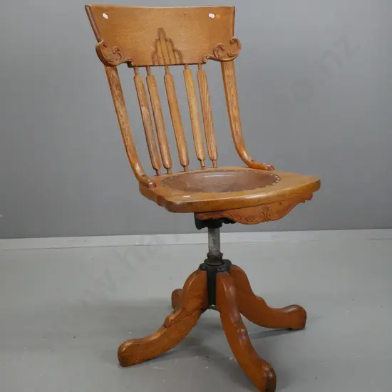 vintage revolving oak desk chair, slatted back w/ shaped crest, leather seat embossed wreath w/ helmet & sword. On 4-pt