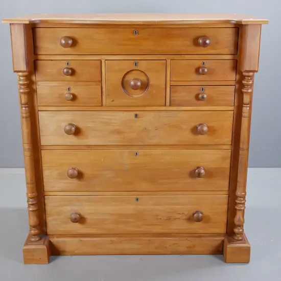 vintage rimu 8-drawer chest with turned columns and wooden knobs, brass escutcheons, on plinth base. Split to one side,