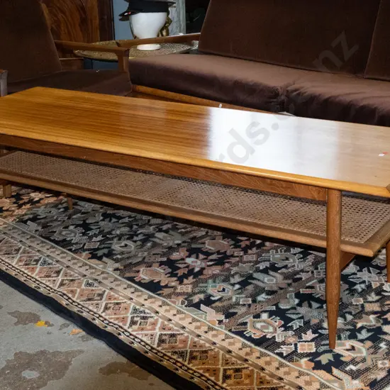 retro mahogany coffee table on turned legs, with cane inset magazine shelf, cross-banded edges. Loose leg joints, fading