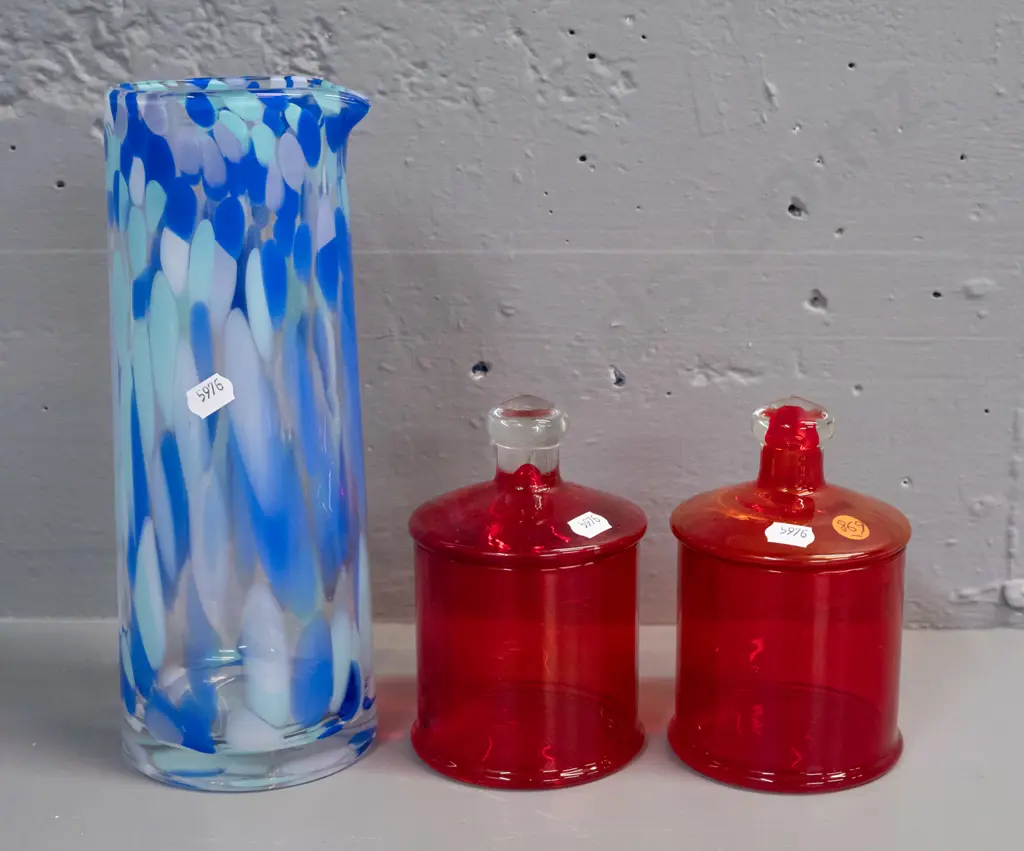 3 glass items - 2 red lidded canisters, one with clear knob, and a blue mottled art glass tall vase or jug with pouring Image 1++