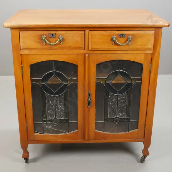 Edwardian rimu cupboard with 2 drawer, 2 leadlight cupboard doors, with panelled sides, on casters. One cracked piece of