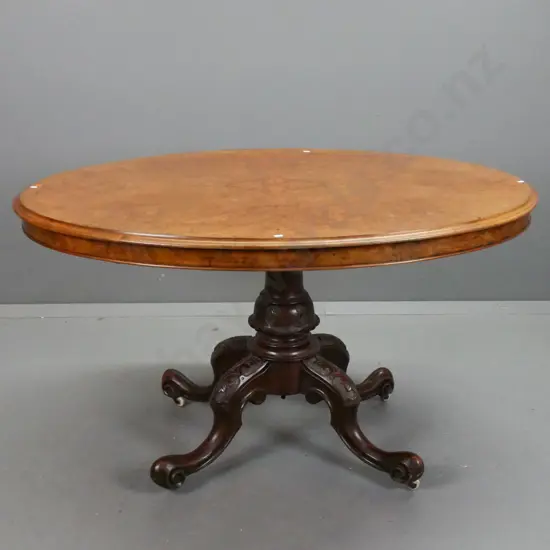Victorian walnut oval loo table on column base w/ 4 carved scrolling legs, porcelain casters, working tilt top, slight