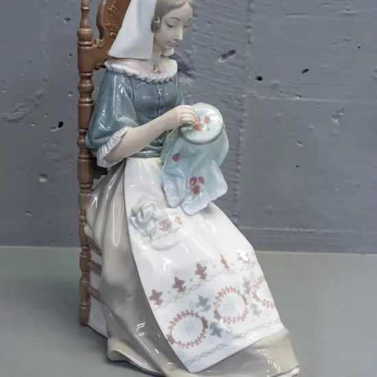 Lladro figure - woman with needlework seated in chair H-280 L-210 front to back