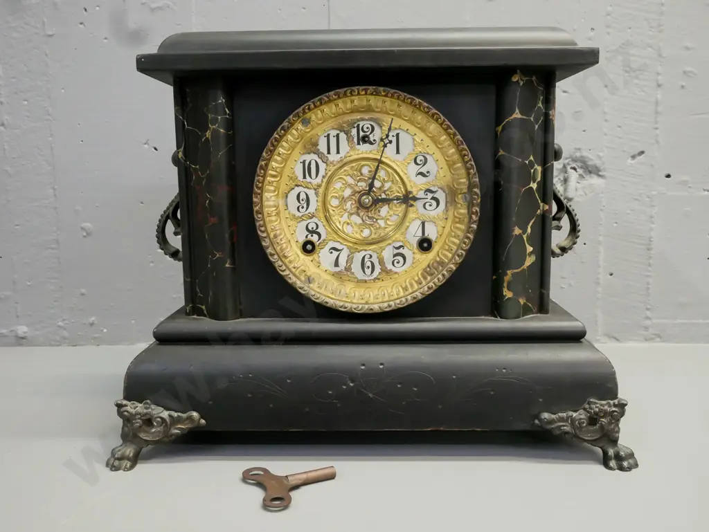 ebonised wooden mantel clock w/ marbled corners, applied scrolling cast handles, paw feet, gilded face. Gilbert Clock Co Image 1++