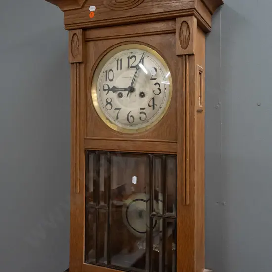 vintage oak-cased chiming wall clock w/ silvered dial marked Stewart Dawson & Co, brass bezel. Bevelled leadlight door,
