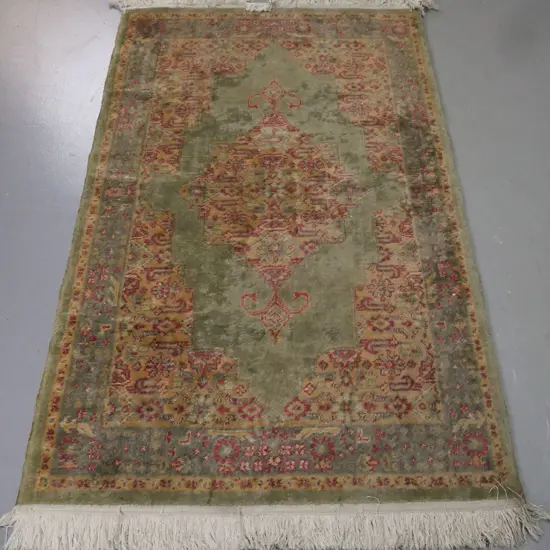 Persian-style floor rug, green ground w/ red & camel geometric & floral borders. Some fading, stains & discolouration.