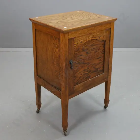 vintage oak bedside cabinet with panelled sides and door with drop handle, square legs on spade feet & metal casters -