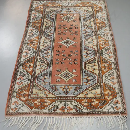 hand knotted geometric pattern wool floor rug with braided fringes - pale blues, pinks and browns - some wear