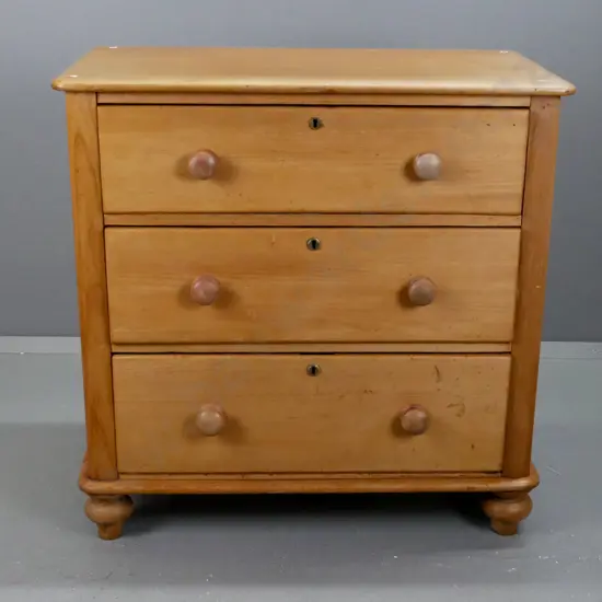 New Zealand colonial kauri 3-drawer round-cornered chest on bun feet w/brass locks and escutcheons, wooden knobs. Splits
