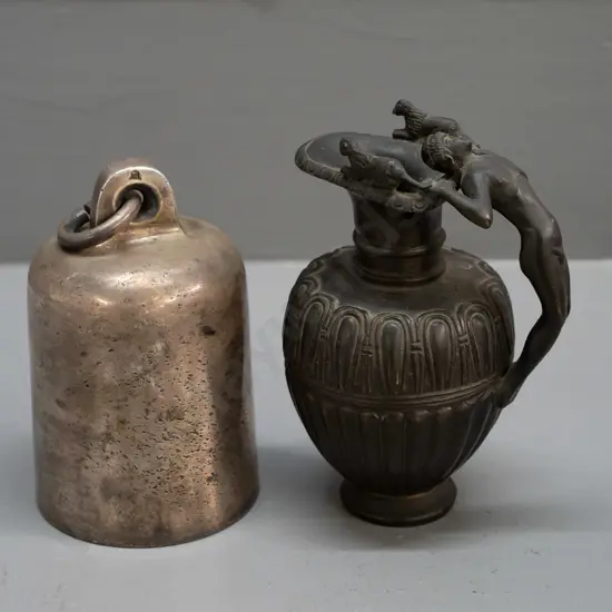 small cylindrical cast metal bell, no ringer, and a heavy cast brass urn jug with figural handle with bronze patina