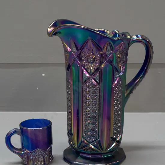 2 irridescent purple/blue carnival ware jugs - large one is H-210 W-180 handle to spout