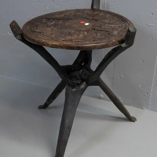 collapsible African carved hardwood table with tripod base, elephants and other animals in top, some cracks and drilled