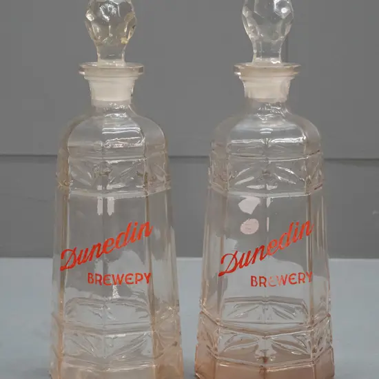 pair of clear glass stoppered decanters marked "Dunedin Brewery" - one with staining inside, minor wear to lettering on