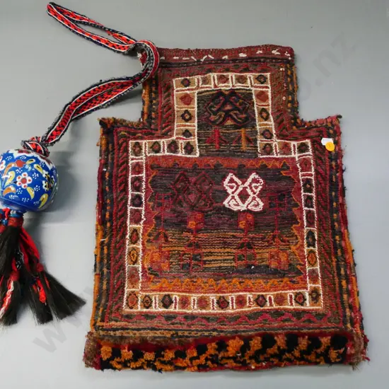 hand-woven middle-eastern bag with narrow opening and a ceramic bauble on woven strap with horsehair tassels