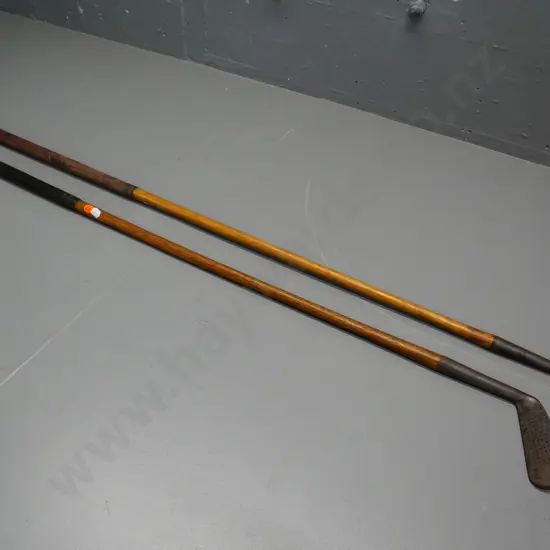 2 vintage golf clubs with wooden stems and leather grips