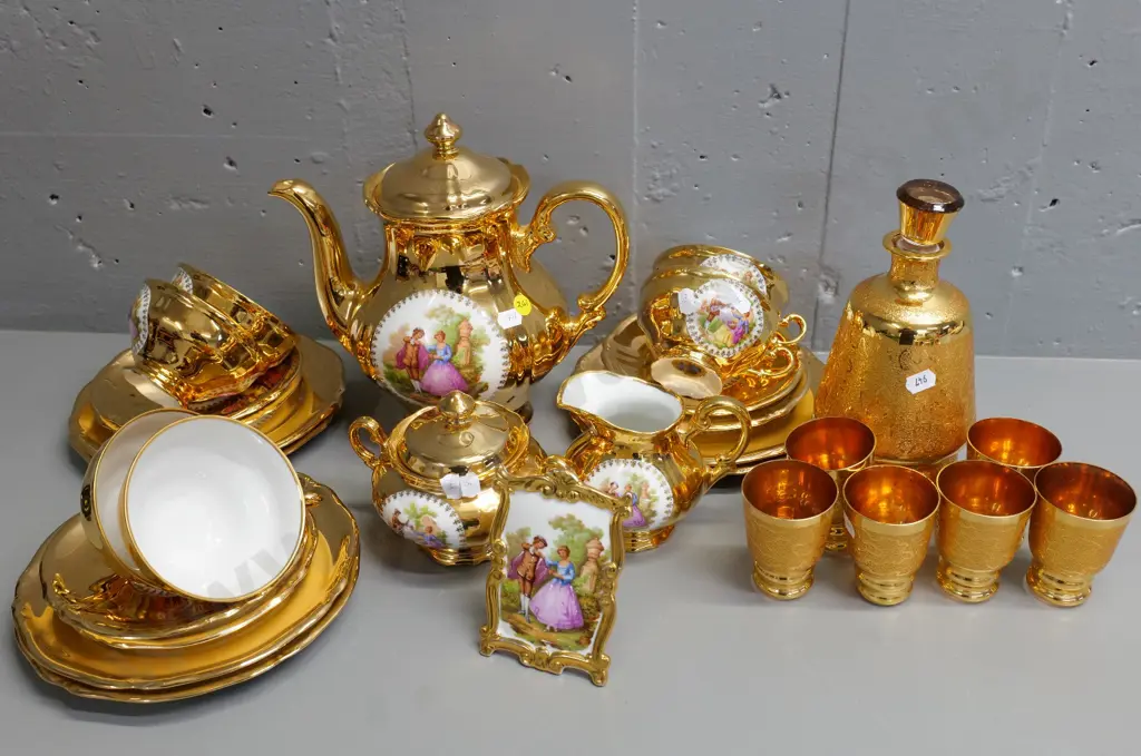 gilt china: German romance scene 21-piece tea set, 7-piece decanter set (fault to rim) and a Limoges plaque Image 1++