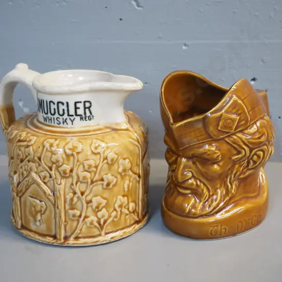 2 whisky jugs: Old Smuggler w/Port Dundas stamp on base, has chip off relief decoration H170 W200, and McCallum